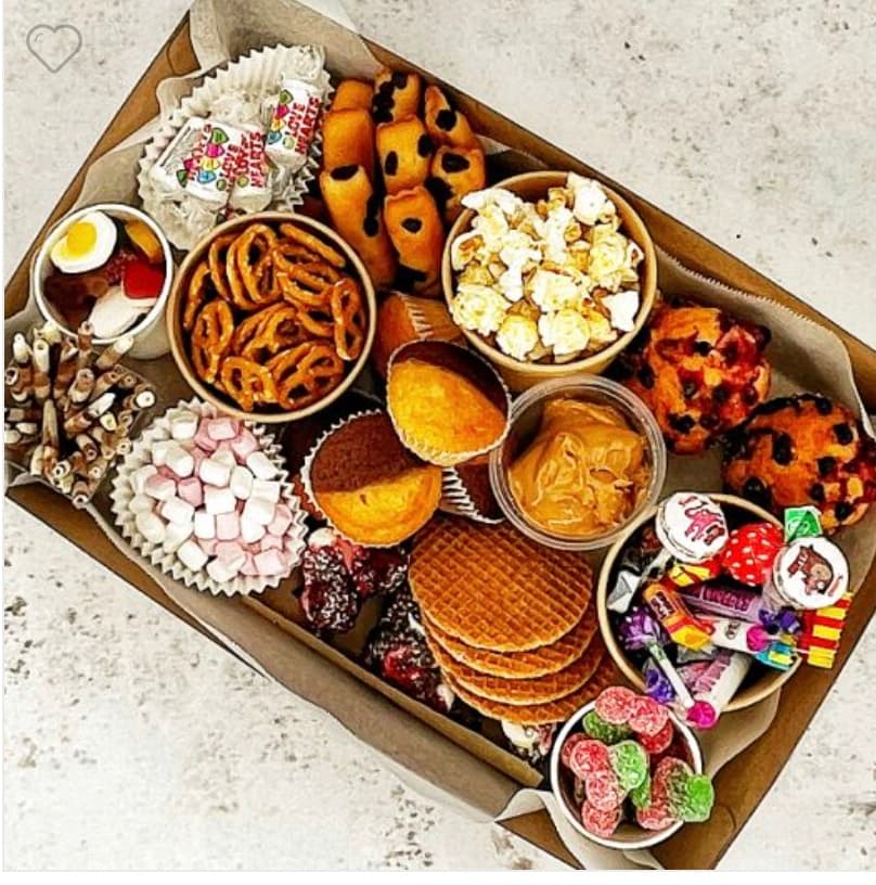 Cardboard box filled with pretzels, popcorn, muffins, stroopwafels, marshmallows, and various colorful candies.