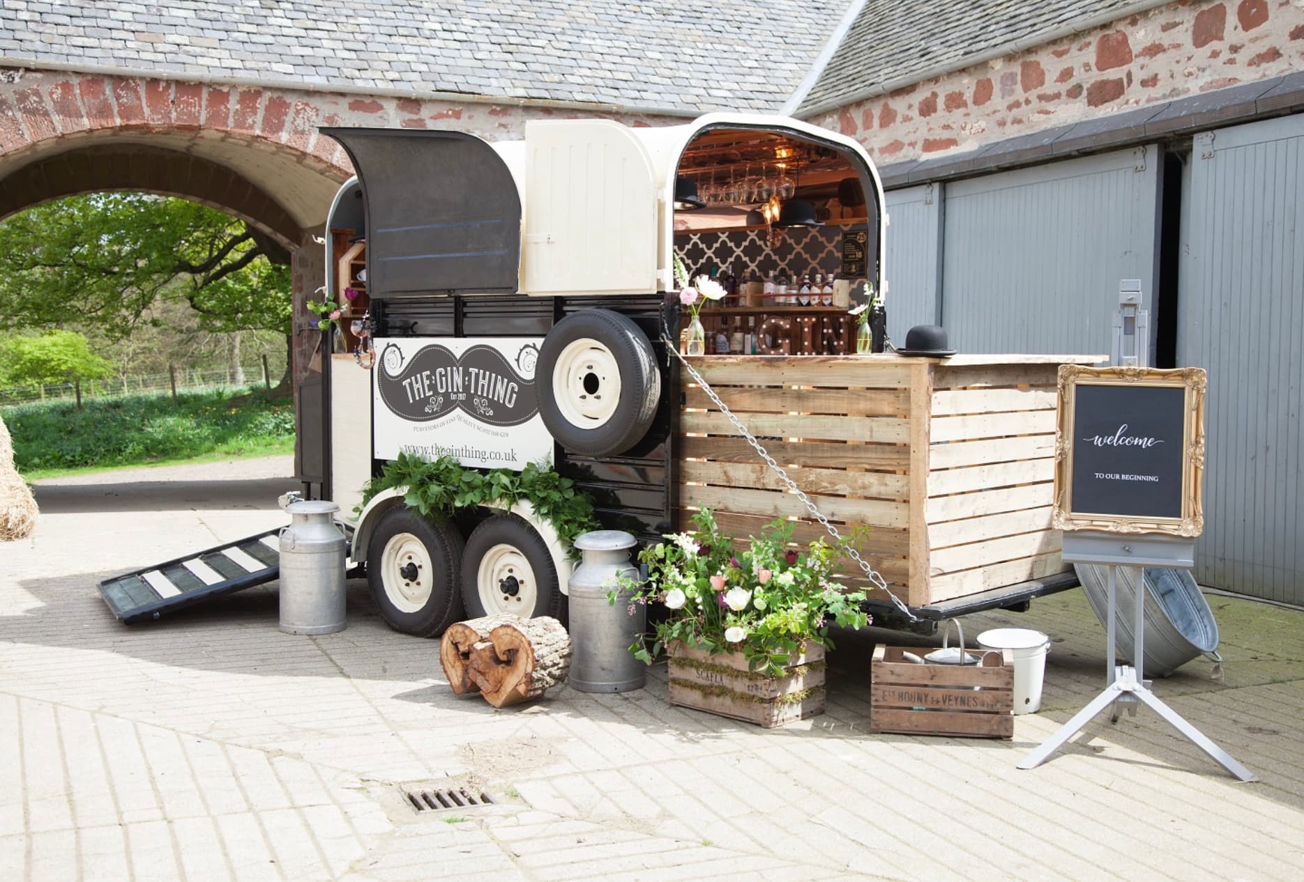 Vintage horse trailer converted into a mobile gin bar with rustic wooden counters and fresh flowers.